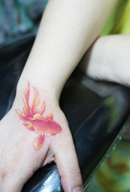 Dziewczęca ręka w kształcie klasycznego wzoru tatuażu małych złotych rybek