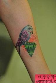 Jentearm med et fargerikt tatoveringsmønster for fugl og diamant