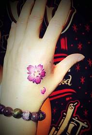 en rød liten blomster tatovering på baksiden av hånden