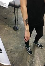 Fotografi e hollë e tatuazhit me një trëndafil të zi në parakrahin e djathtë të njeriut
