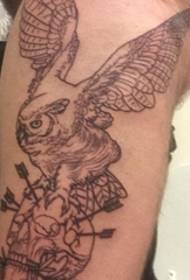 Black-gray owl on arm grabs arrow thorns skull tattoo