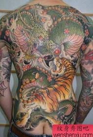 Espalda masculina con un patrón de tatuaje de batalla de dragón y tigre dominante y genial