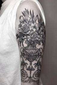 Brațul fetei pe o vază cu plante negre și poza tatuajului de flori