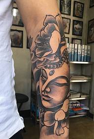 czarno-szary tatuaż na ramieniu w połączeniu z lotosem i Buddą