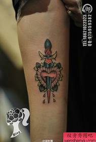 Flickans arm med en liten dolk och älskar tatueringsmönster