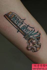 Түрлі түсті кілтпен және әріптермен татуировкасы бар қыздың қолы