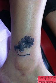 a small black and white four-leaf clover tattoo pattern at the ankle of the girl